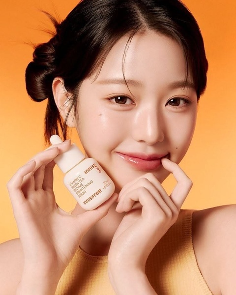 This ad creative features a clean, studio-lit portrait of a model holding a brightening serum, using a warm monochromatic color palette to emphasize skin health and product efficacy.
